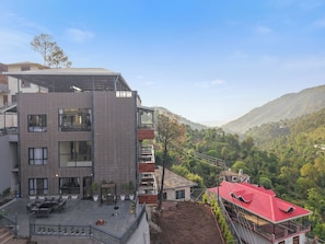 Un immeuble à plusieurs étages doté d’un espace-terrasse sur le toit, d’un balcon et offrant une vue sur un paysage vallonné.
