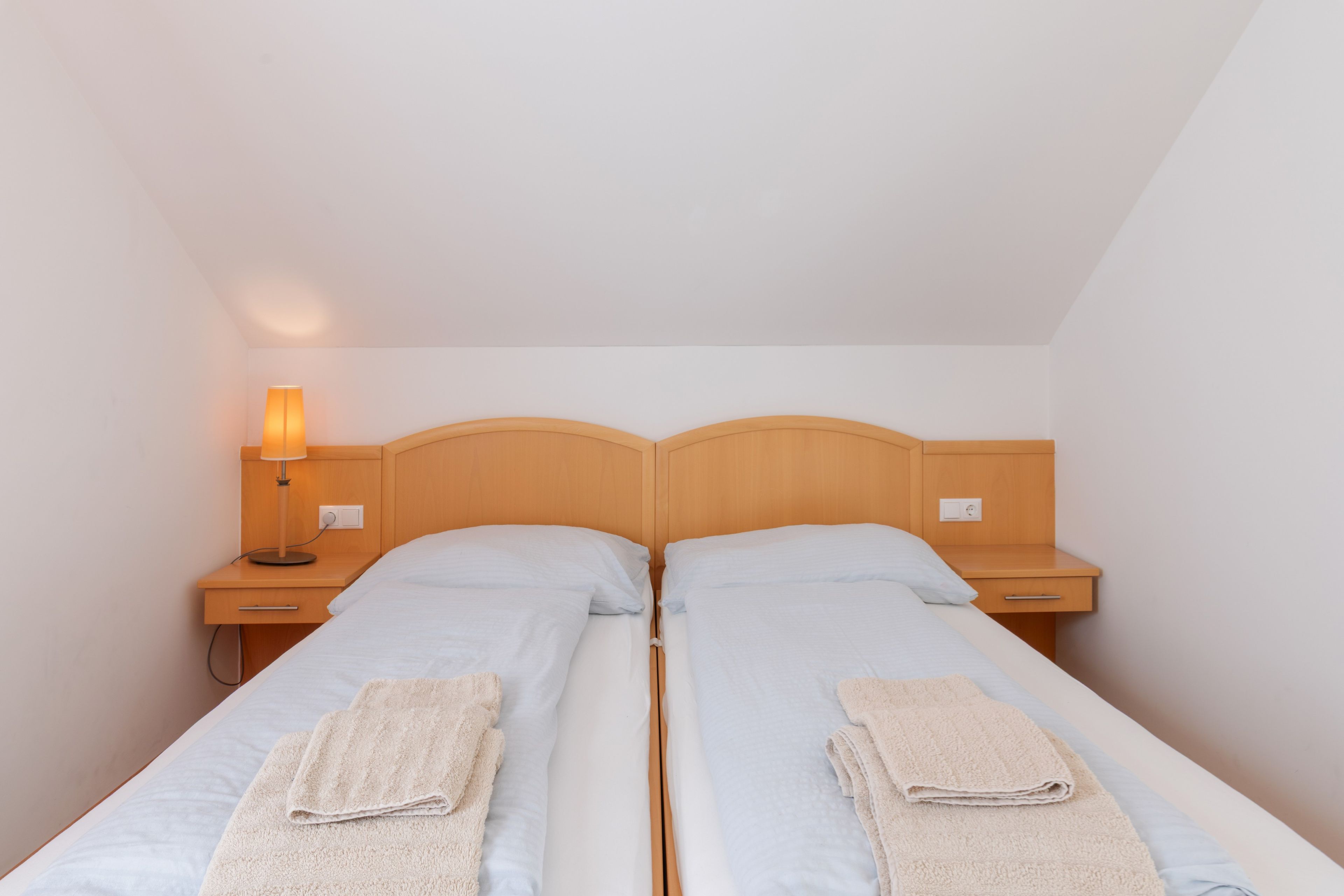 A twin room with two beds, a nightstand with a lamp, and a drawer.
