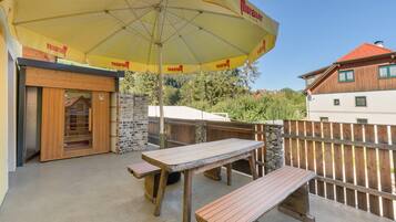 Un espace extérieur aménagé en terrasse, avec des tables et des bancs en bois, un parasol jaune et un mur en briques.
