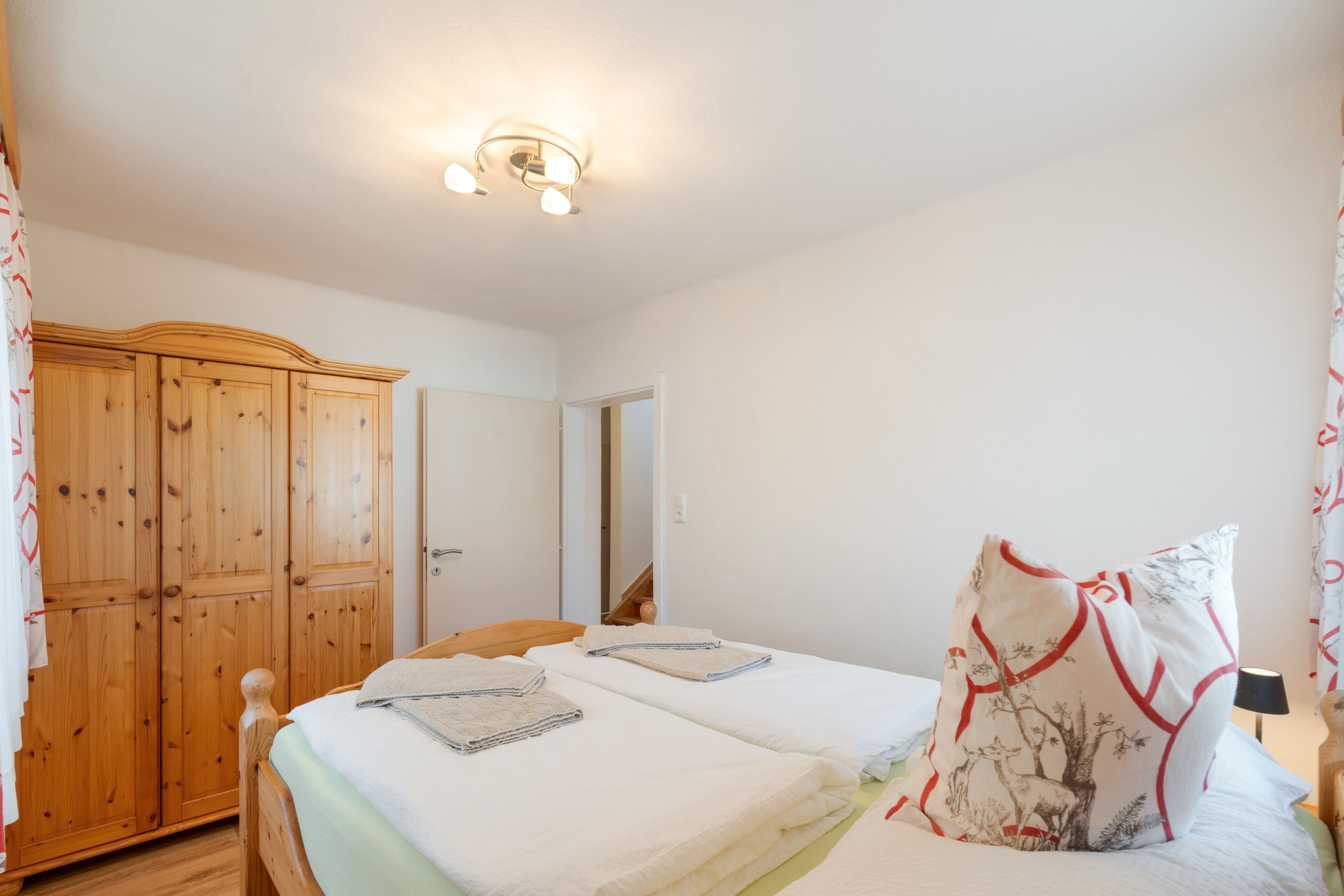 Een slaapkamer met twee bedden, een houten garderobe en een plafondlamp.