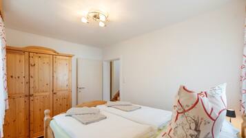 Een slaapkamer met twee bedden, een houten garderobe en een plafondlamp.