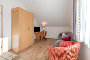 A room with a large wardrobe, a desk with a chair, a sofa with cushions, and a window with curtains. - Holiday Home 'Ma-inz.eu' with Mountain View, Private Terrace & Wi-Fi (Steindorf)