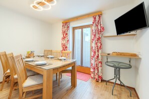 A dining area with a wooden table, chairs, and a television mounted on the wall.