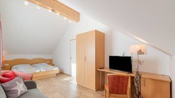 Ein modernes, helles Zimmer mit einem Bett, einem Schreibtisch, einem Sessel und einem Fernseher.