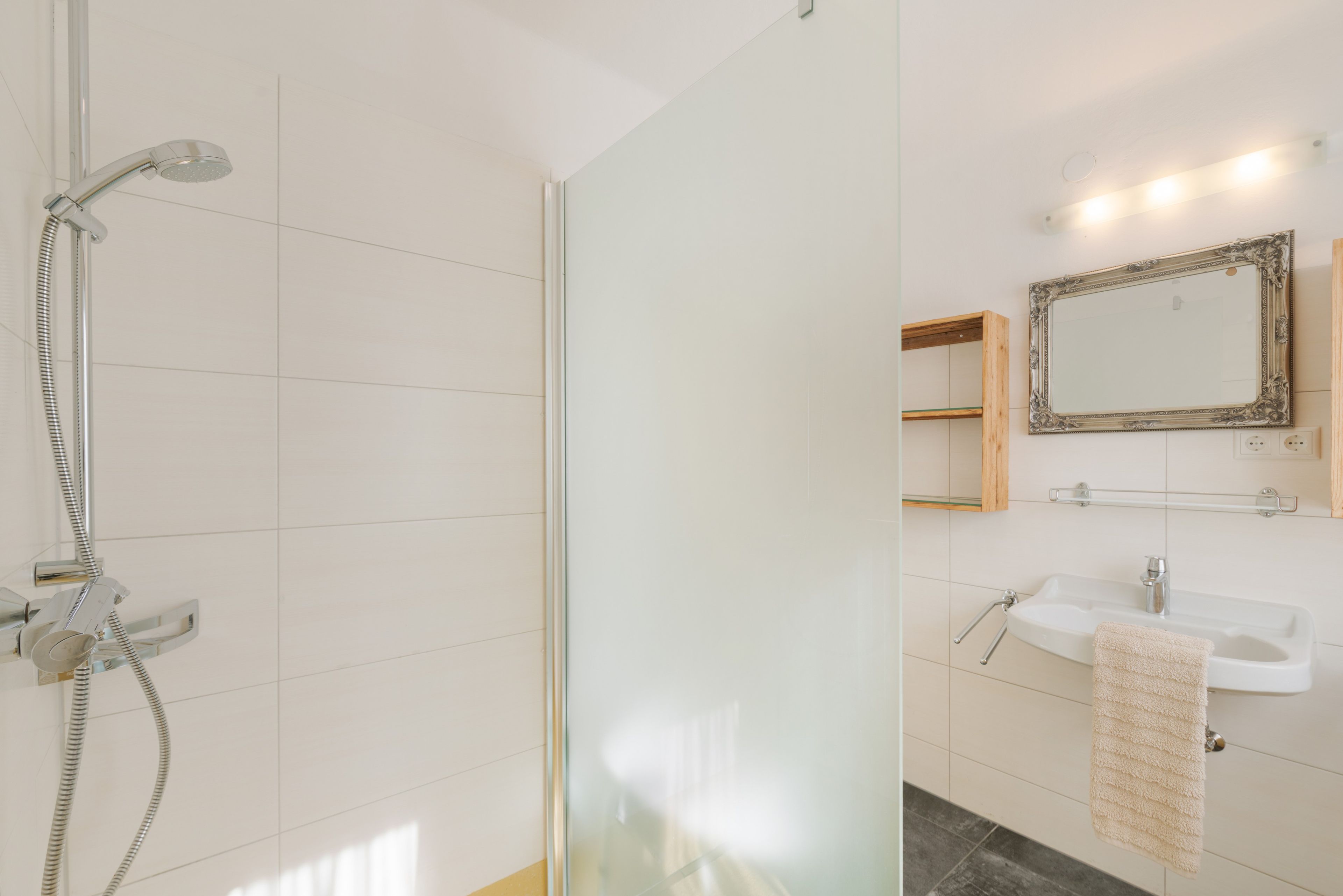 Un baño moderno con cabina de ducha de vidrio, un lavabo blanco y un espejo con marco decorativo.