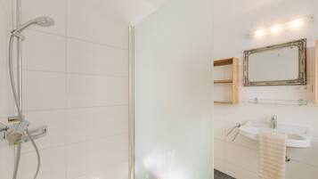Un baño moderno con cabina de ducha de vidrio, un lavabo blanco y un espejo con marco decorativo.