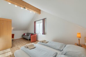 A bedroom with a sloped ceiling, a bed, a chair, a wardrobe, and a window with curtains.