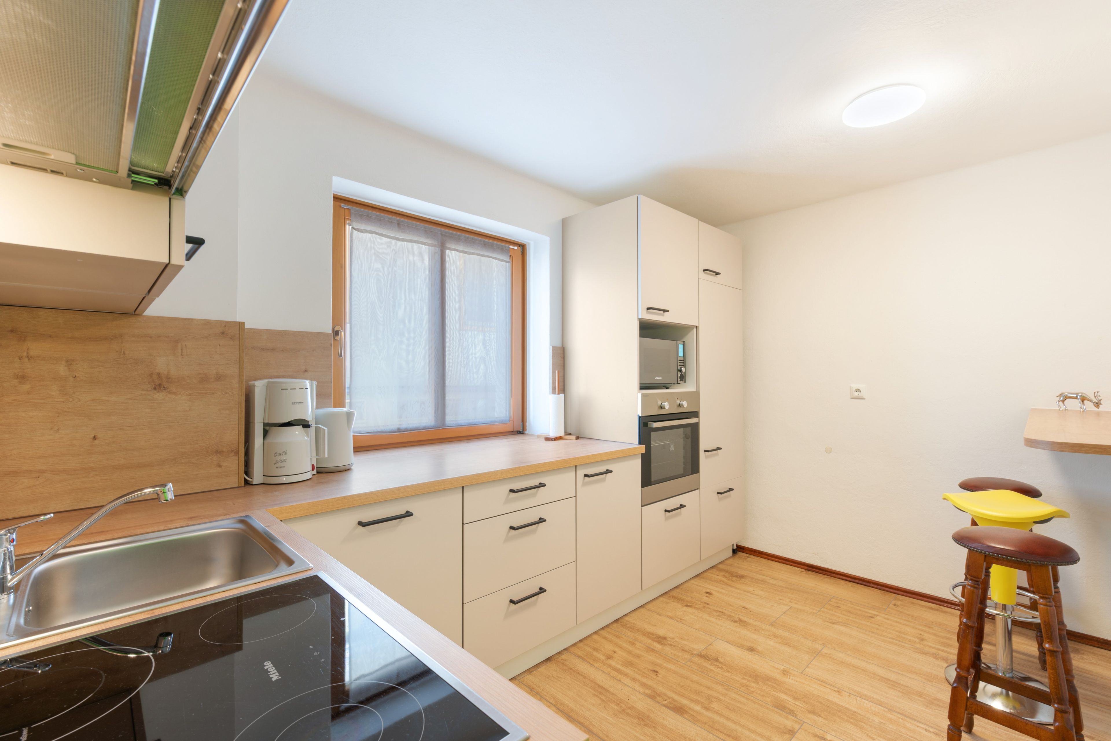 A modern kitchen with a built-in oven, a coffee maker, and a window with a wooden frame.