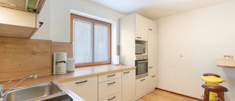 A modern kitchen with a built-in oven, a coffee maker, and a window with a wooden frame.