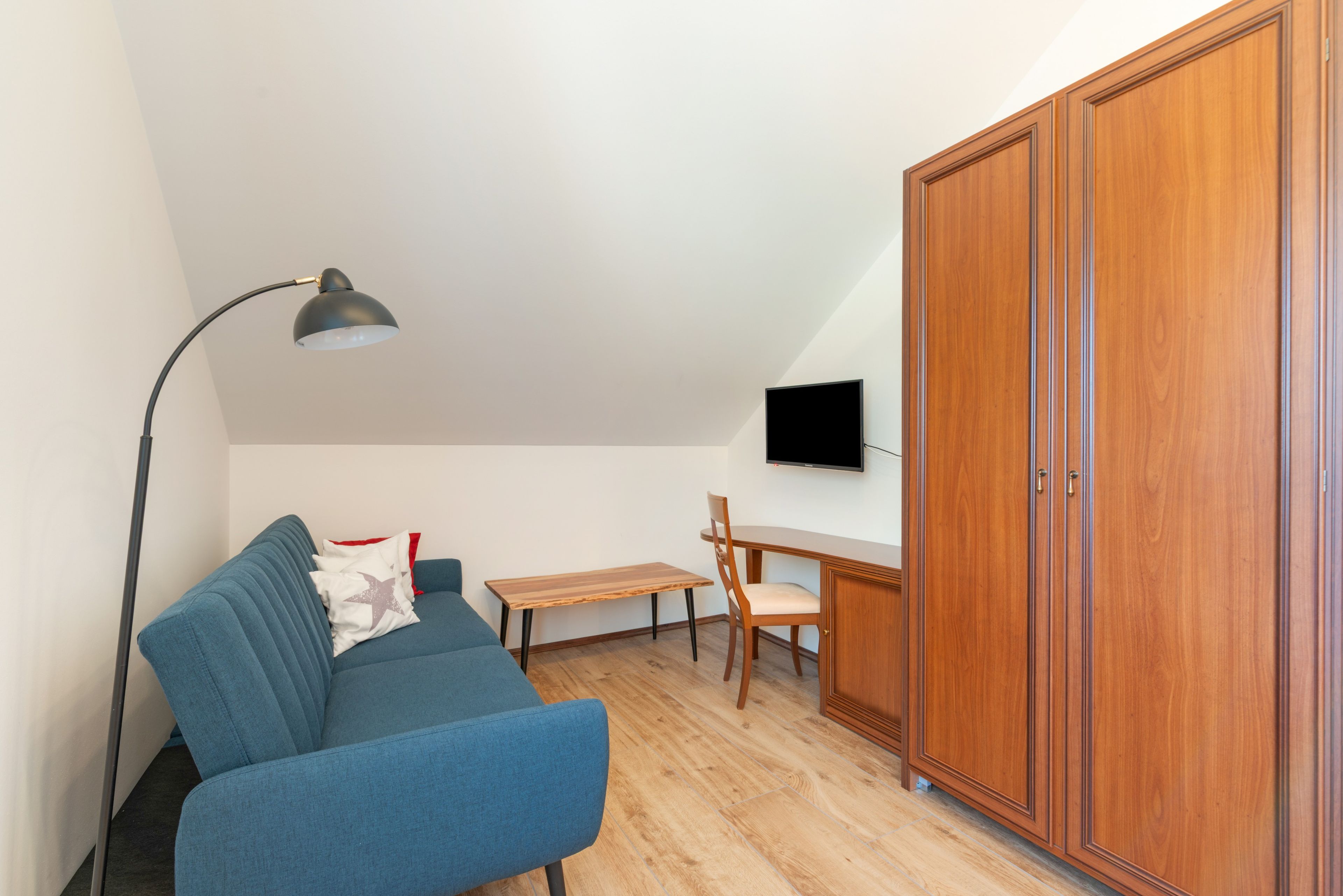 A room with a blue sofa, a wooden table, a wooden wardrobe, and a ceiling lamp.