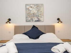 A neatly made bed with a pillow, a wall-mounted painting, and two wall lamps. - The Forge (Falmouth)