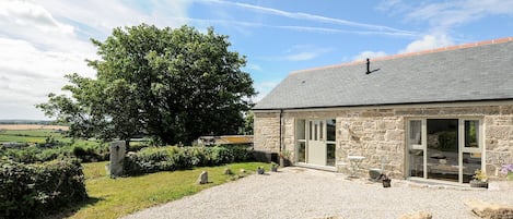 A stone building with a gravel driveway, a large tree, and a clear sky.
