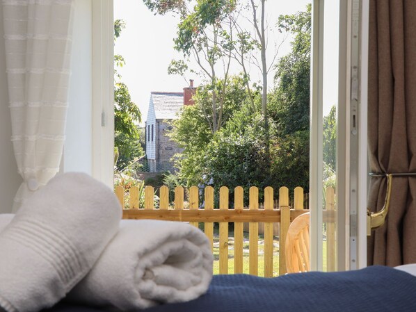Ein Zimmer mit Bett, einem fensterbelaubten Fenster und Blick auf einen Holenzaun und viel Grün draußen.