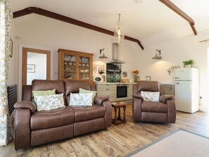 Ein Wohnzimmer mit zwei braunen Ledersofas, einem kleinen Holztisch, einer Küche mit einem weißen Kühlschrank und einer Pendelleuchte.