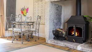 A stone fireplace with a black stove, a dining table with chairs, and a vase with flowers. - The Forge (Falmouth)