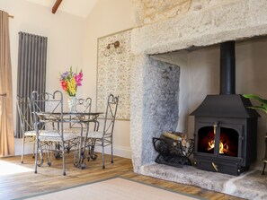 A stone fireplace with a black stove, a dining table with chairs, and a vase with flowers. - The Forge (Falmouth)