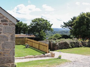 Un edificio de piedra con terraza de madera, un sendero de grava y vistas a un valle boscoso.