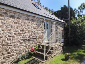 Ein Steinhaus mit Metalltreppe, einer Tür und einem kleinen Garten mit Blumentöpfen.
