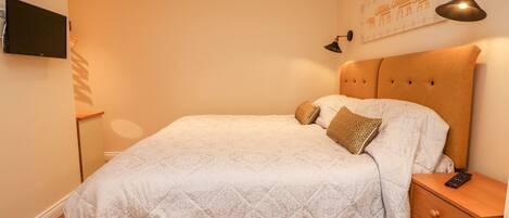A neatly arranged bedroom with a bed, a bedside table, a wall-mounted TV, and a lamp.