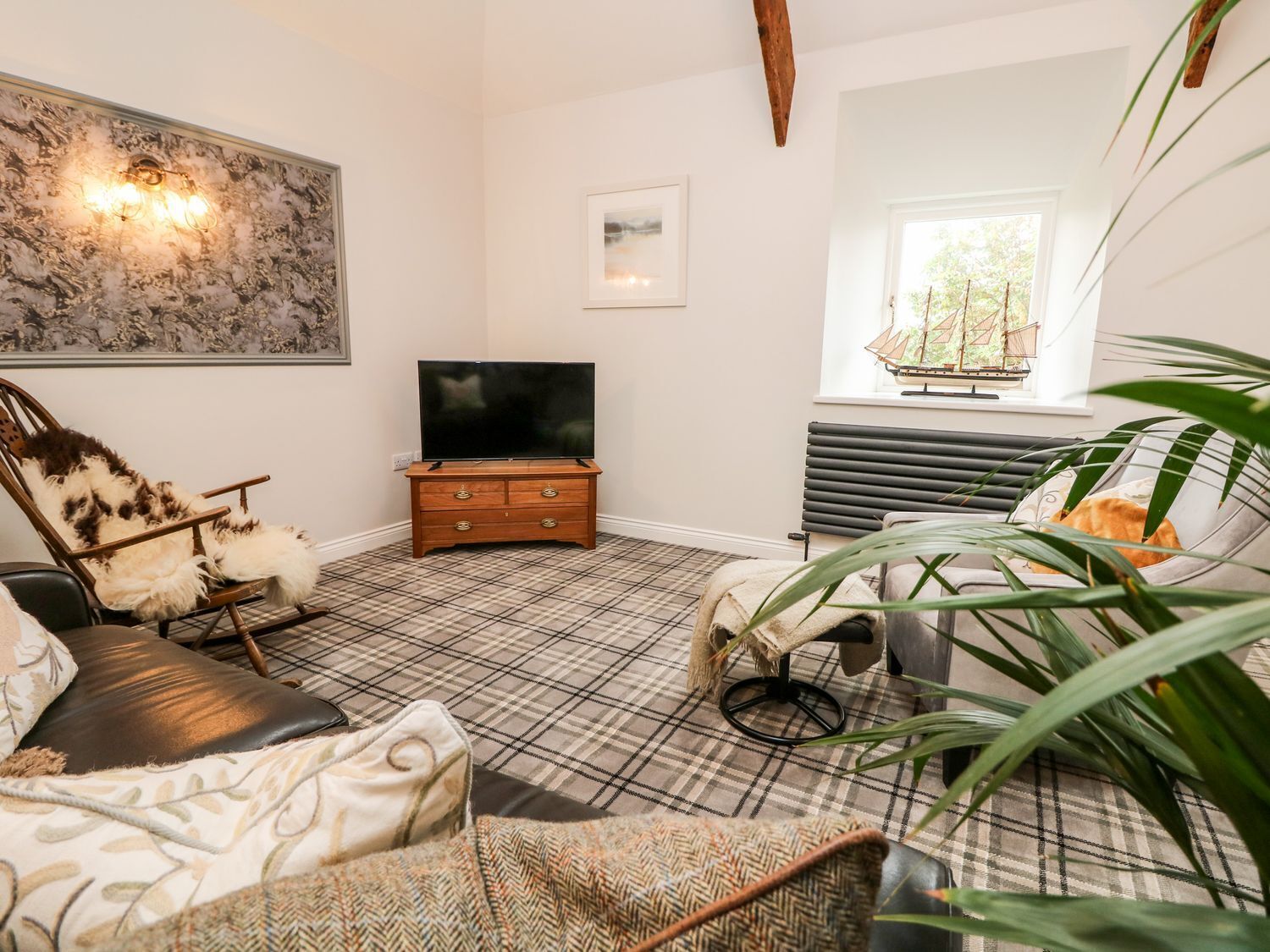 A cozy living room with a plaid floor, a television, a fireplace, and a window with a ship model.