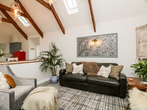 Ein Wohnzimmer mit einer schwarzen Ledersofa, einem karierten Teppich, einer Topfpflanze und einem großen abstrakten Gemälde an der Wand.