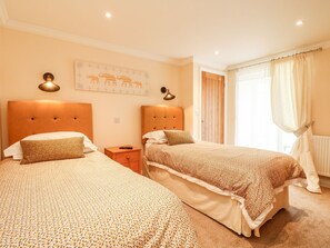 Une chambre d’hôtel avec deux lits, une table de chevet, une lampe fixée au mur, une porte et une fenêtre avec des rideaux.