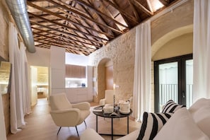 A spacious living area with a high wooden ceiling, a stone wall, and a balcony with curtains.