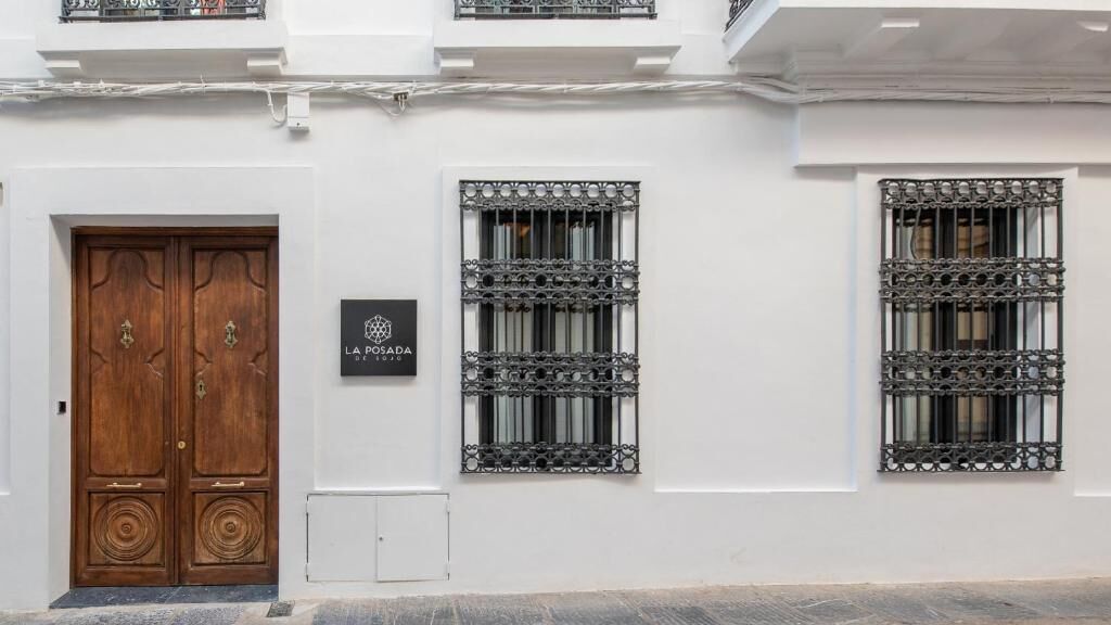 Fachada de edificio con puerta de madera doble, dos ventanas con rejas decorativas y una placa con texto.
