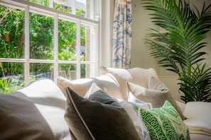 Ein Bett mit Kissen, ein Fenster mit Blick ins Grüne und ein Blumentopf.