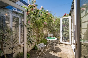 Eine Terrasse mit Tisch und Stühlen, eine Glastür und ein Garten mit Kletterpflanzen.