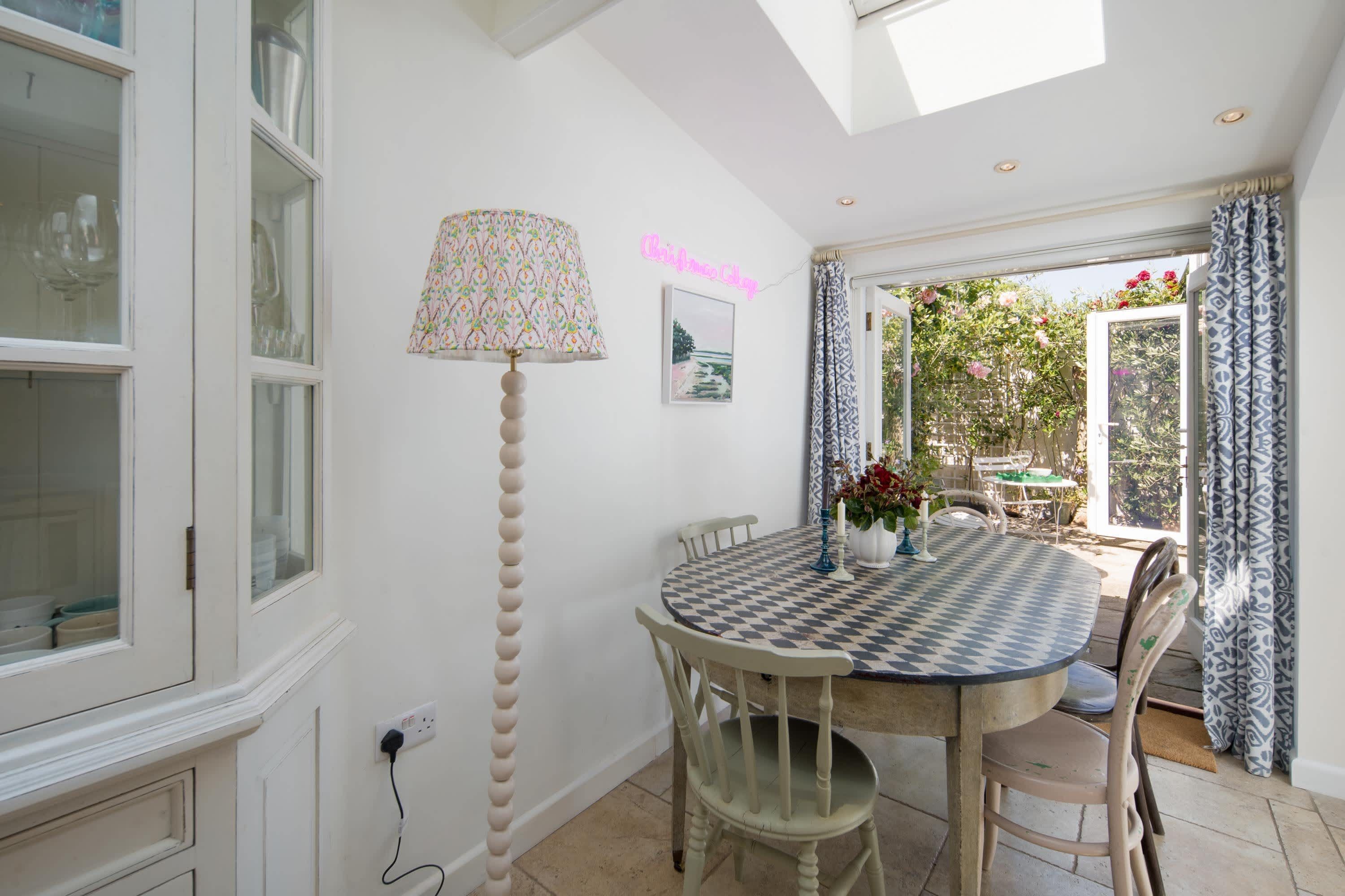 Un coin repas avec une table à carreaux, des chaises, une lampe et une vue sur un jardin par la fenêtre.