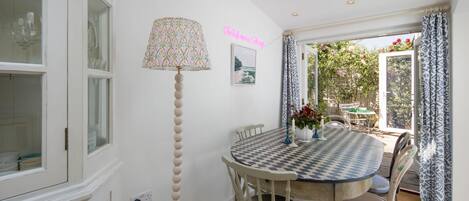 Un coin repas avec une table à carreaux, des chaises, une lampe et une vue sur un jardin par la fenêtre.