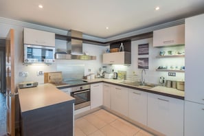 A modern kitchen with a built-in oven, microwave, and stainless steel range hood. - Marina View Stylish 2 Bed Waterfront in Cowes (Cowes)