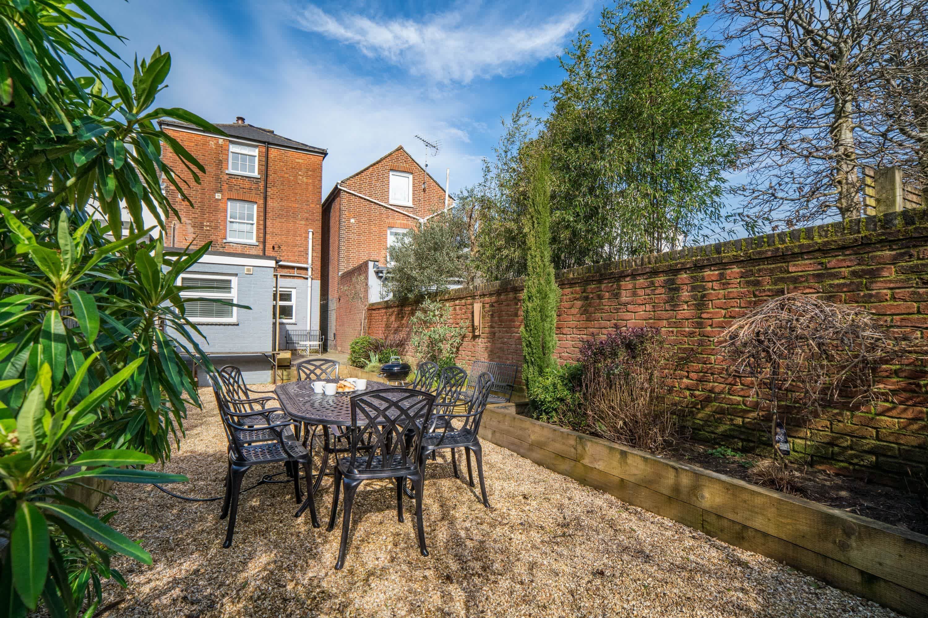 A patio with a table and chairs, a brick wall, and a garden.