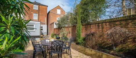A patio with a table and chairs, a brick wall, and a garden.