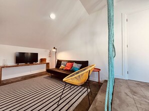 Un salon moderne avec un canapé, un téléviseur, une lampe, un fauteuil en osier et un tapis à rayures.