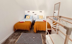 Une petite pièce étroite, avec deux lits, une armoire en bois, un tapis à motifs et un miroir.