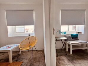 A room with a white table, a wicker chair, a small table with a lamp, and a bench with cushions. - Apartment, Portas Residence (Ponta Delgada)