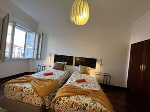 Une chambre double avec deux lits, une grande fenêtre et un luminaire suspendu moderne.