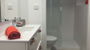 Un baño con un lavabo blanco, un espejo, una toalla roja, una ducha con puerta de vidrio y un tapete verde.