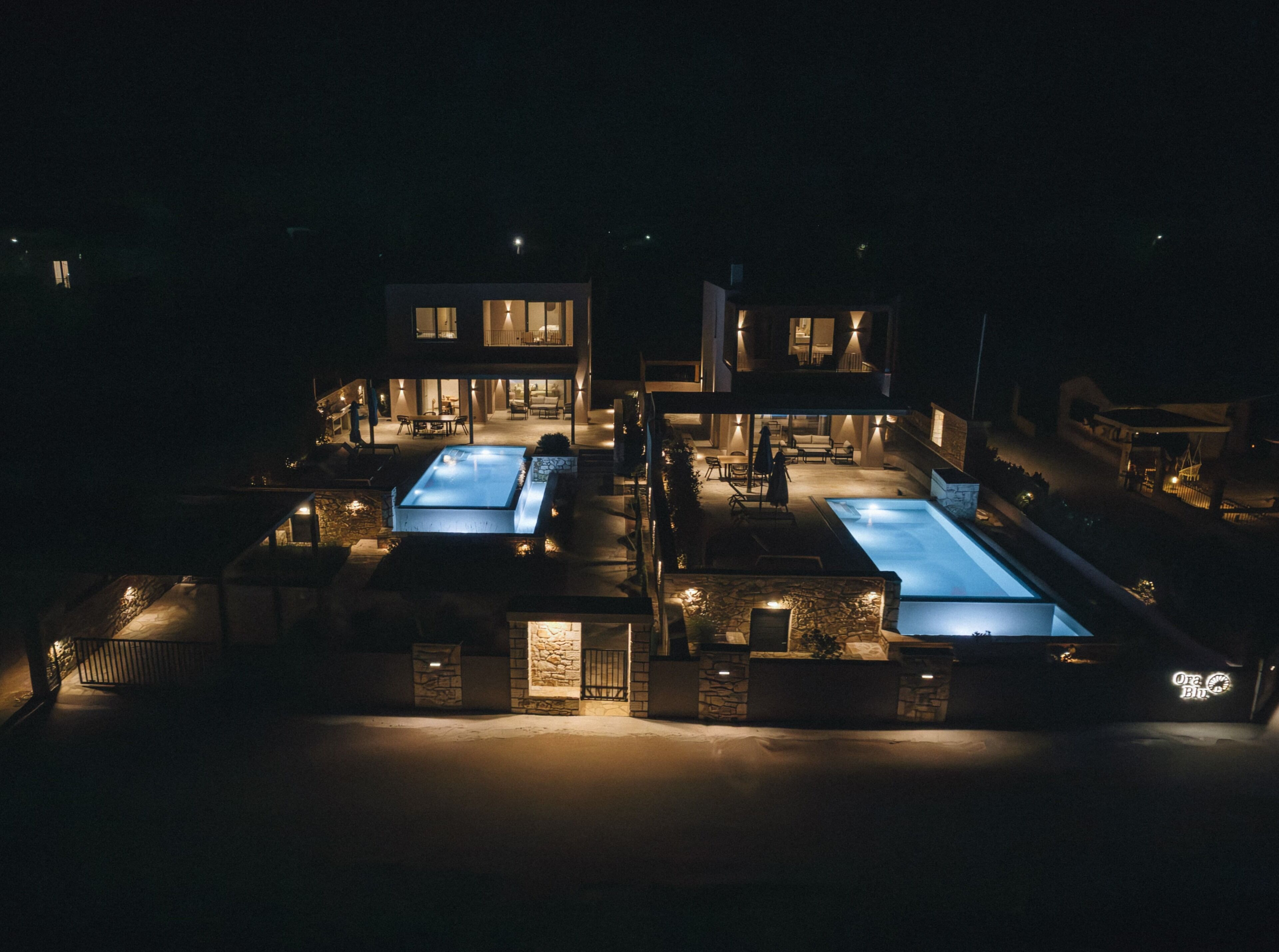 A modern two-story house with a swimming pool, outdoor seating, and a well-lit patio area.