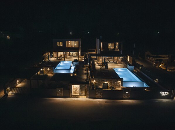Una casa moderna de dos pisos con piscina, mobiliario exterior y un patio bien iluminado.