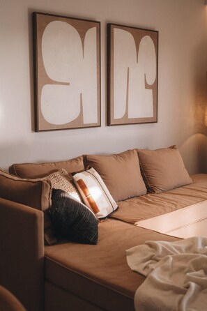 Una habitación con un sofá marrón, dos cuadros enmarcados y una manta en el suelo.