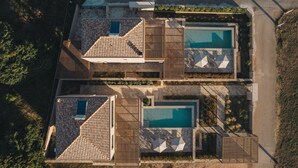 Eine Luftaufnahme eines Anwesens mit zwei Schwimmbecken, einer überdachten Terrasse und einer Steinfassade.