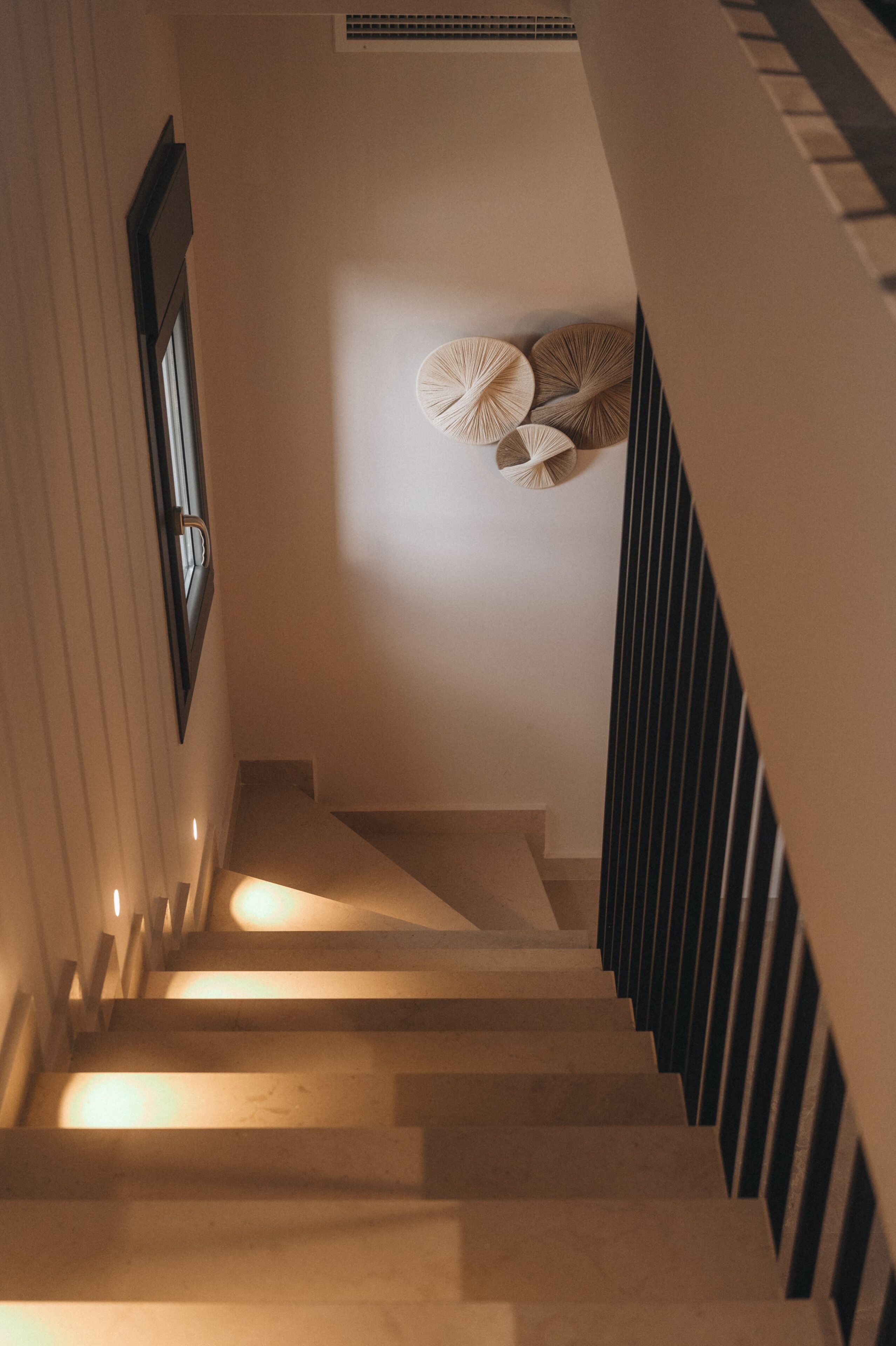 Una escalera con barandilla, un aplique de pared y una ventana con persianas.