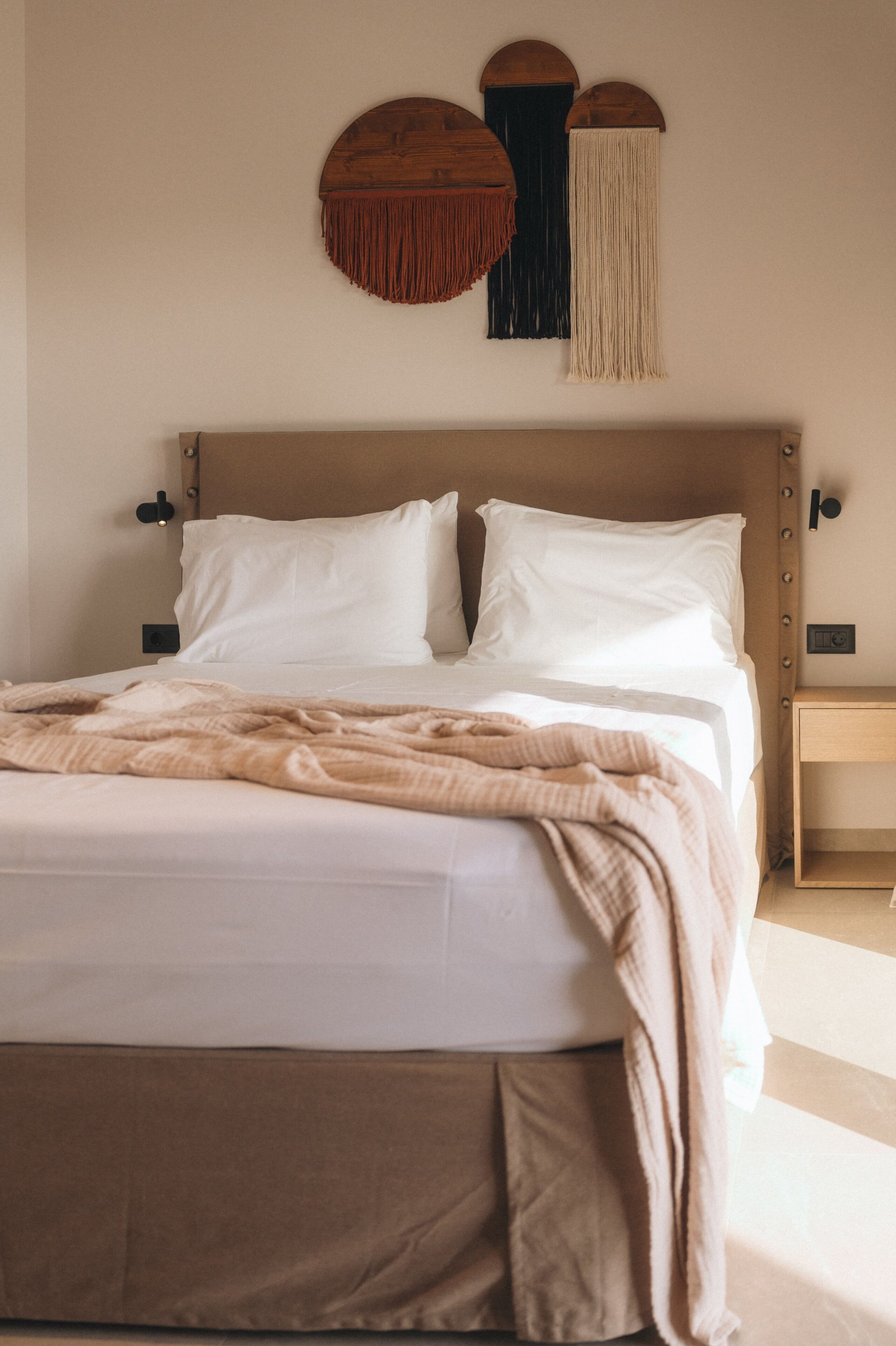A bed with white linens, a beige throw blanket, and a wooden headboard.
