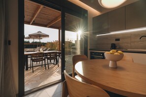 A modern kitchen with a wooden dining table, a bowl of fruit, and a view of the outdoors. - ORA BLU (PREVEZA)