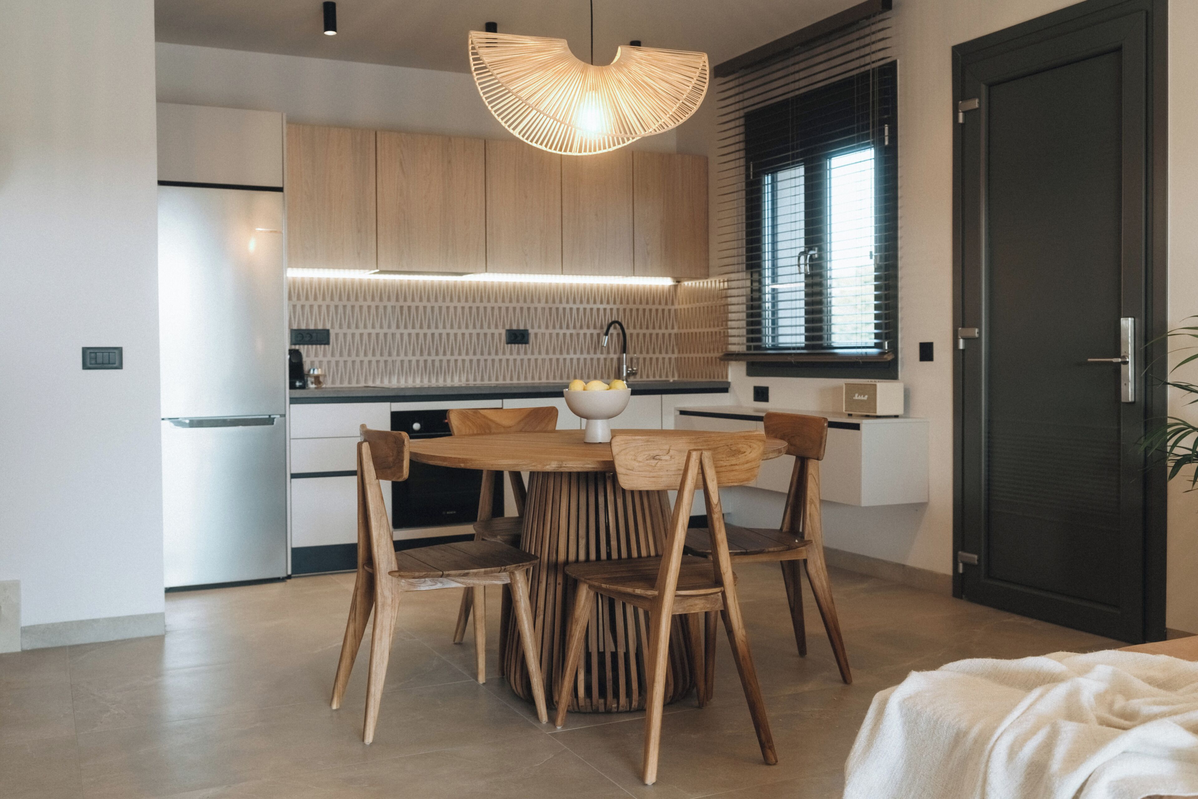 A modern kitchen with wooden cabinets, a round dining table, and a unique pendant light.