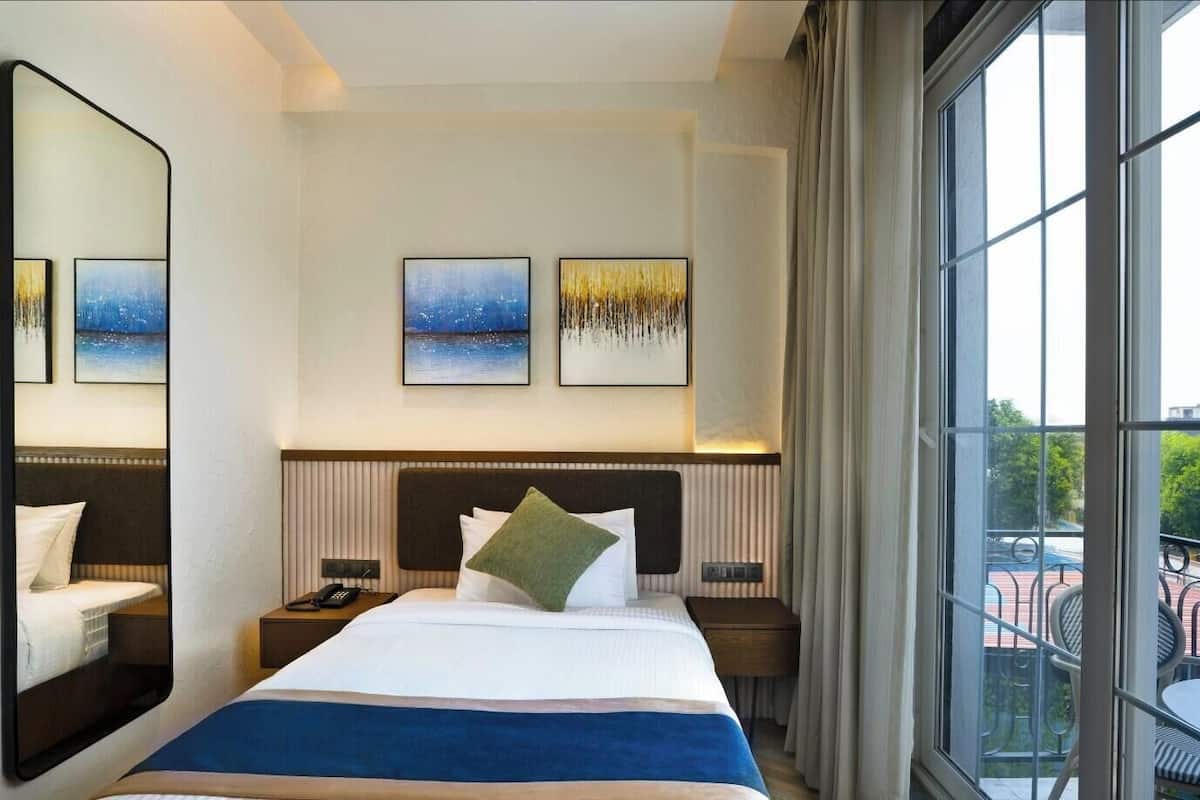 Ein Hotelzimmer mit einem großen Bett, zwei Nachttischen, einem Spiegel und Kunstwerken an der Wand.