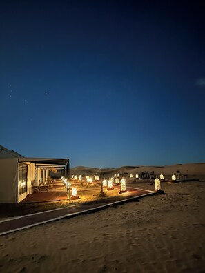 Un hotel en el desierto con fachada de vidrio, mobiliario exterior y faroles iluminados.